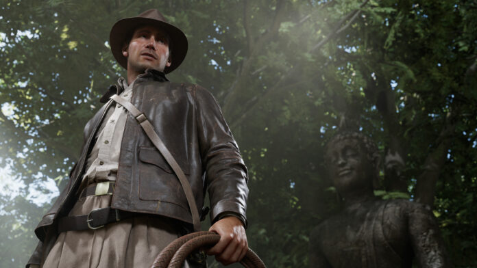 New Indiana Jones Game Indiana Jones in the game Indiana Jones and the Great Circle, standing in a jungle with a rock statue behind him and his whip beside him